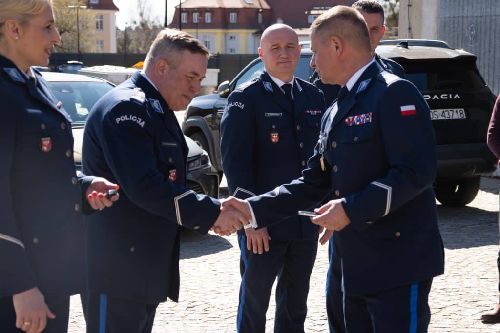 Policjanci podczas oficjalnej prezentacji nowych radiowoz&oacute;w na Mazurach, w tle policyjne pojazdy i budynki.