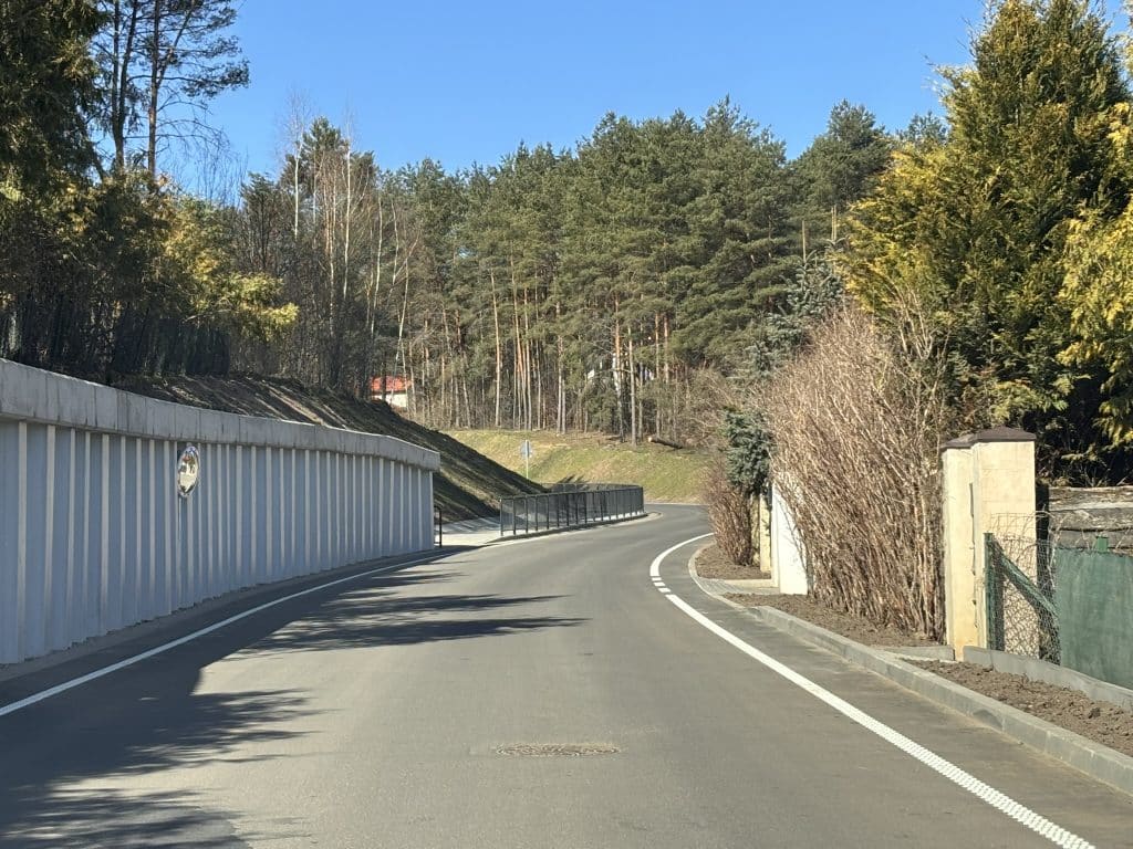 Nowa, wyremontowana droga powiatowa w terenie leśnym, z łagodnym zakrętem i nową barierą ochronną.