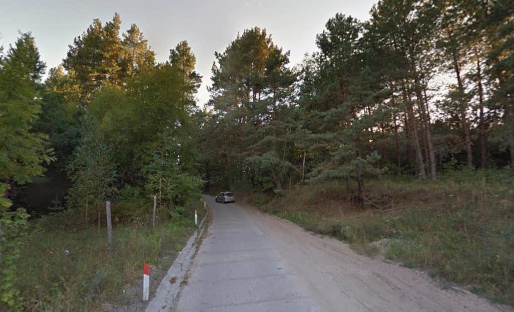 Wąska, zniszczona droga w lesie, kończąca się nowym odcinkiem po remoncie.