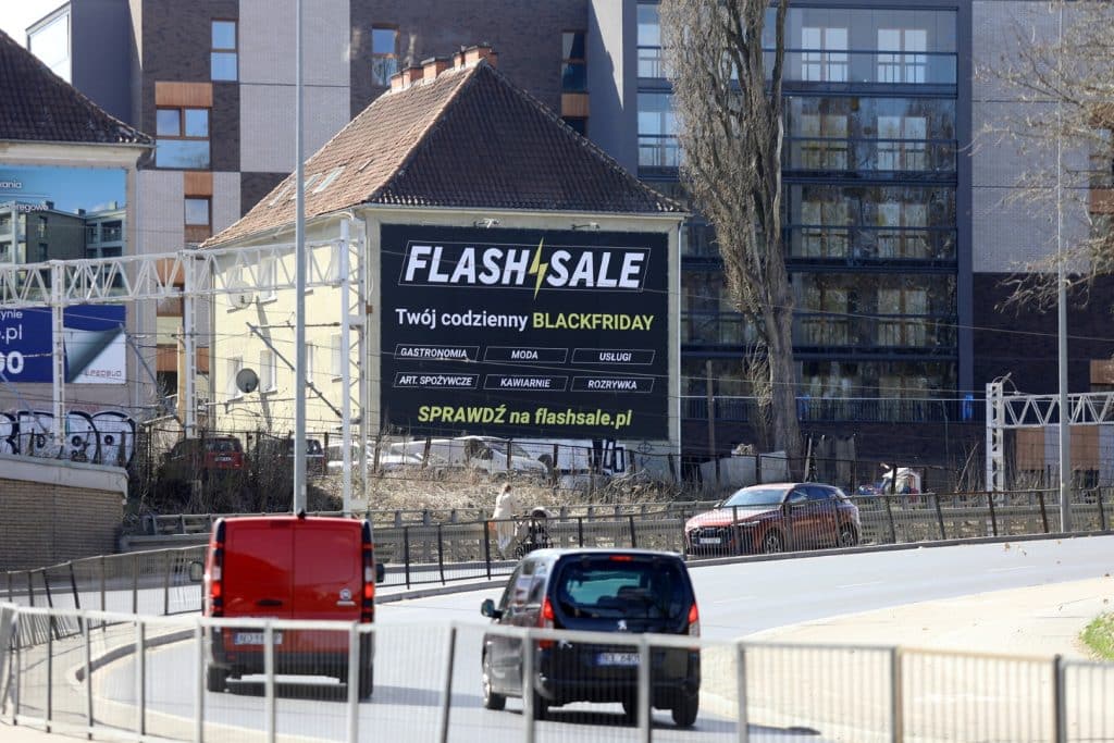 Billboard promujący platformę Flashsale.pl na tle miejskiej ulicy, z hasłem 'Black Friday przez cały rok'.
