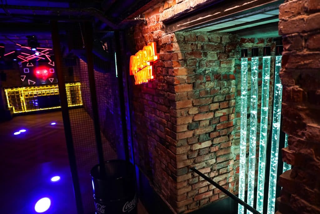 Wnętrze nowego klubu Dyskoteka Music Bar w Olsztynie z ceglaną ścianą i neonowymi światłami.