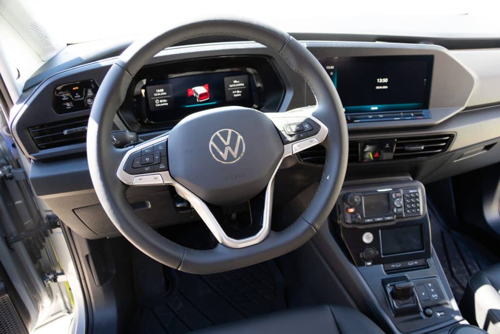 Wnętrze nowoczesnego radiowozu z kierownicą i wyświetlaczami, widoczne elementy wyposażenia pojazdu.