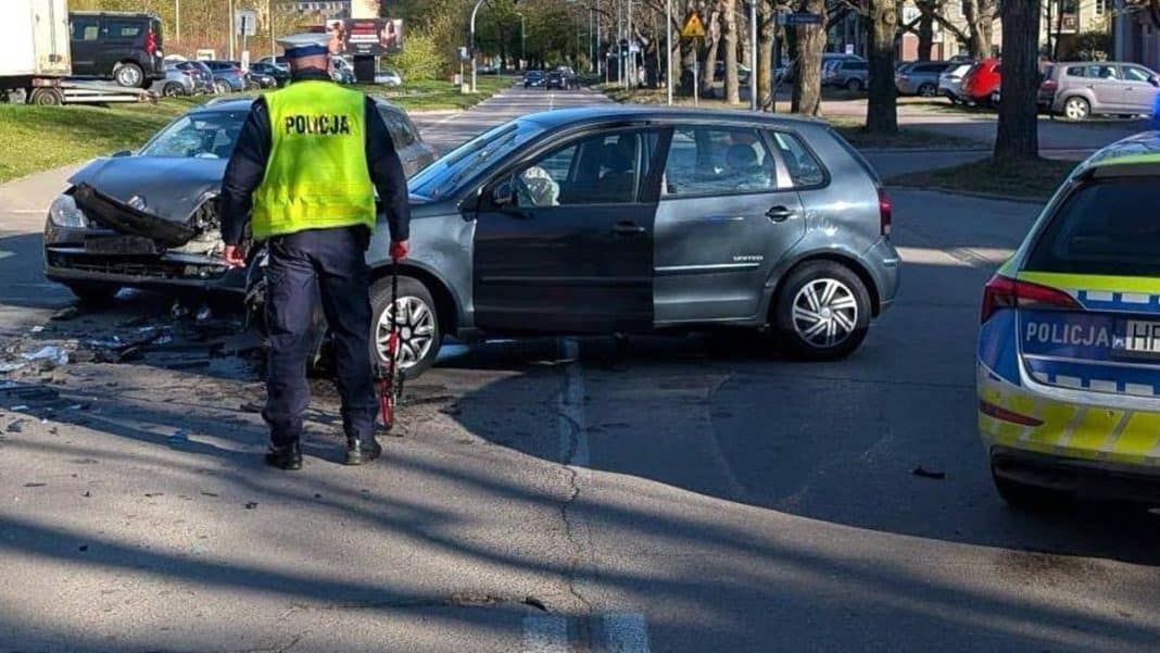 Wypadek na skrzyżowaniu w Ostr&oacute;dzie, z uszkodzonymi samochodami i policjantem na miejscu.