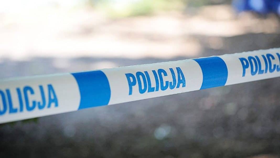 Teren nad jeziorem zabezpieczony przez policję, na pierwszym planie taśma policyjna z napisem 'POLICJA'.