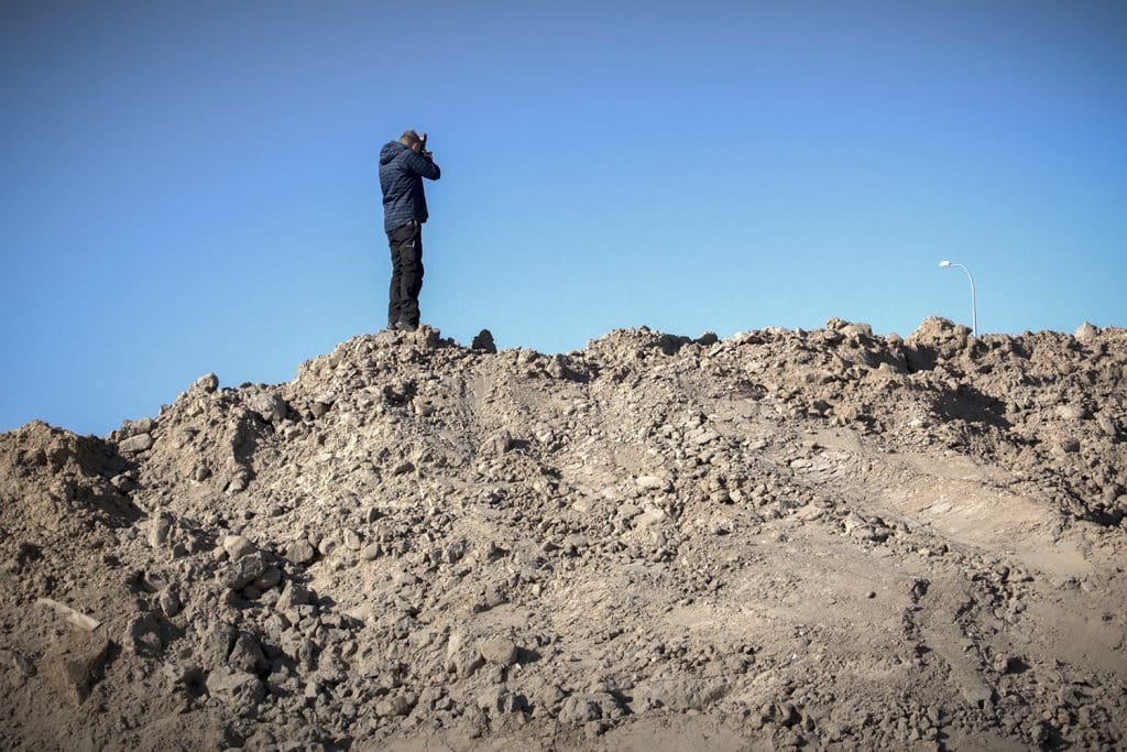 Mężczyzna na wzg&oacute;rzu z ziemi, robiący zdjęcie lub film, w tle bezchmurne niebo.