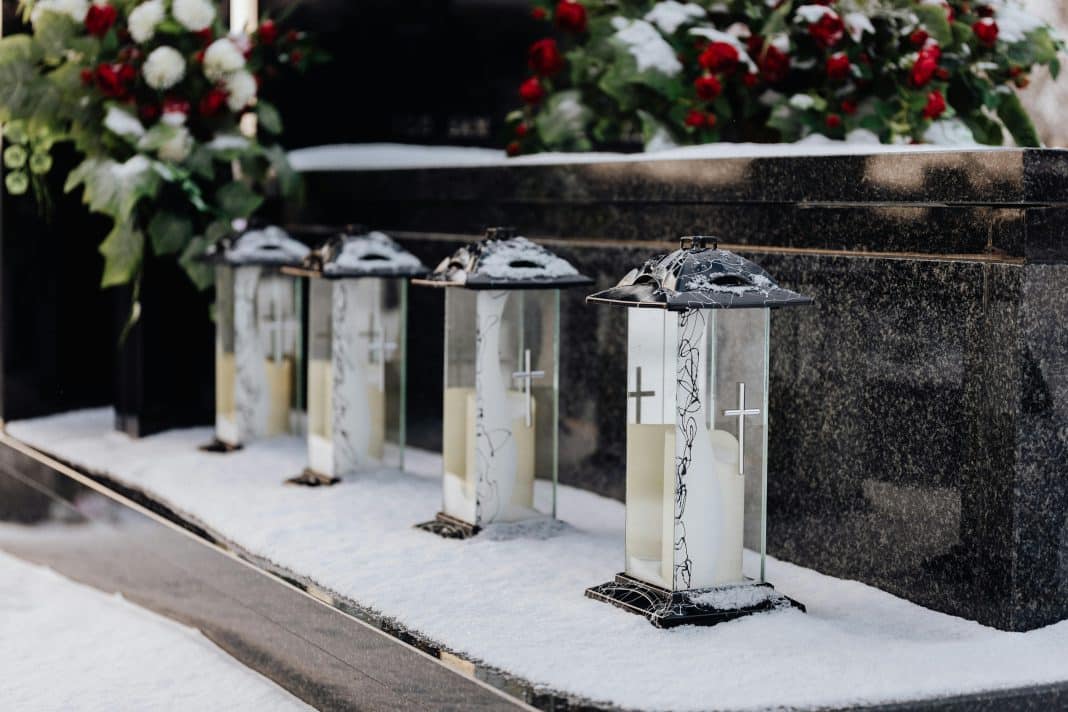 Lampiony i kwiaty na grobie, śnieg wok&oacute;ł, symboliczny obraz pogrzebu.