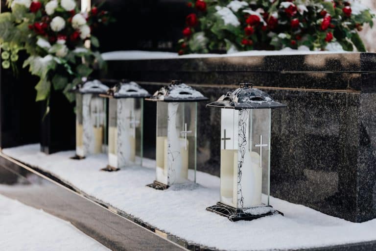 Lampiony i kwiaty na grobie, śnieg wok&oacute;ł, symboliczny obraz pogrzebu.