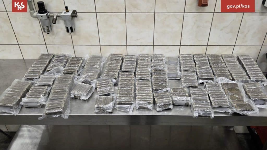 Na zdjęciu widoczne są liczne pakiety ukryte w skrytkach samochodu, zabezpieczone folią, na tle białych płytek.