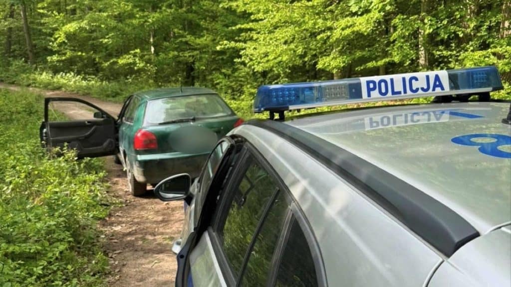 Policja na miejscu kolizji, uszkodzone samochody na leśnej drodze.