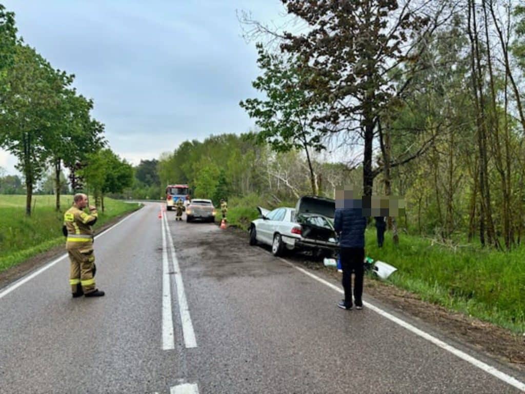 Zdjęcie z miejsca zderzenia na DK16, samochody na poboczu, policjant i strażak przy akcji.