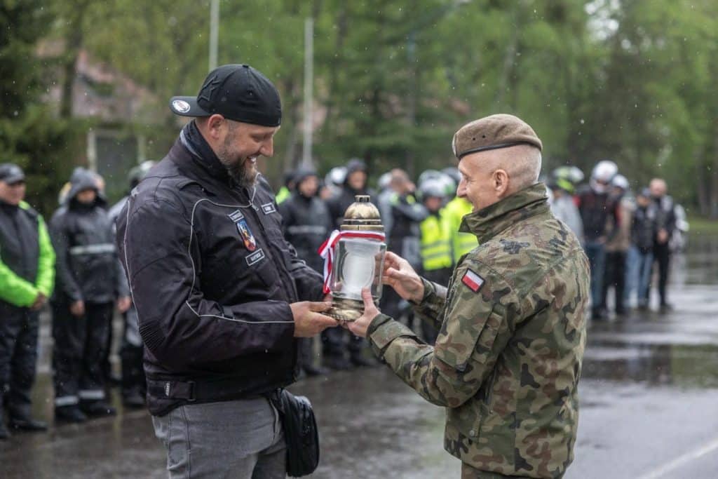 Żołnierz otrzymuje odznaczenie podczas uroczystości święta brygady na tle zgromadzonych żołnierzy i uczestnik&oacute;w.