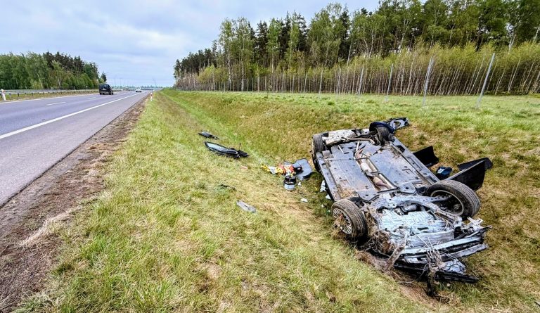 Rozbity samoch&oacute;d leży na poboczu drogi S7 po dachowaniu, w pobliżu rowu, na tle zielonych drzew.