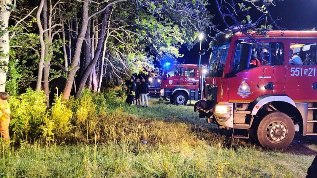 Akcja strażaków przy miejscu dachowania samochodu w lesie nocą.