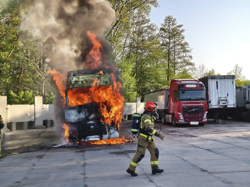 Pożar ciężar&oacute;wki na parkingu w Braniewie, widoczne płomienie i dym, strażak w akcji.