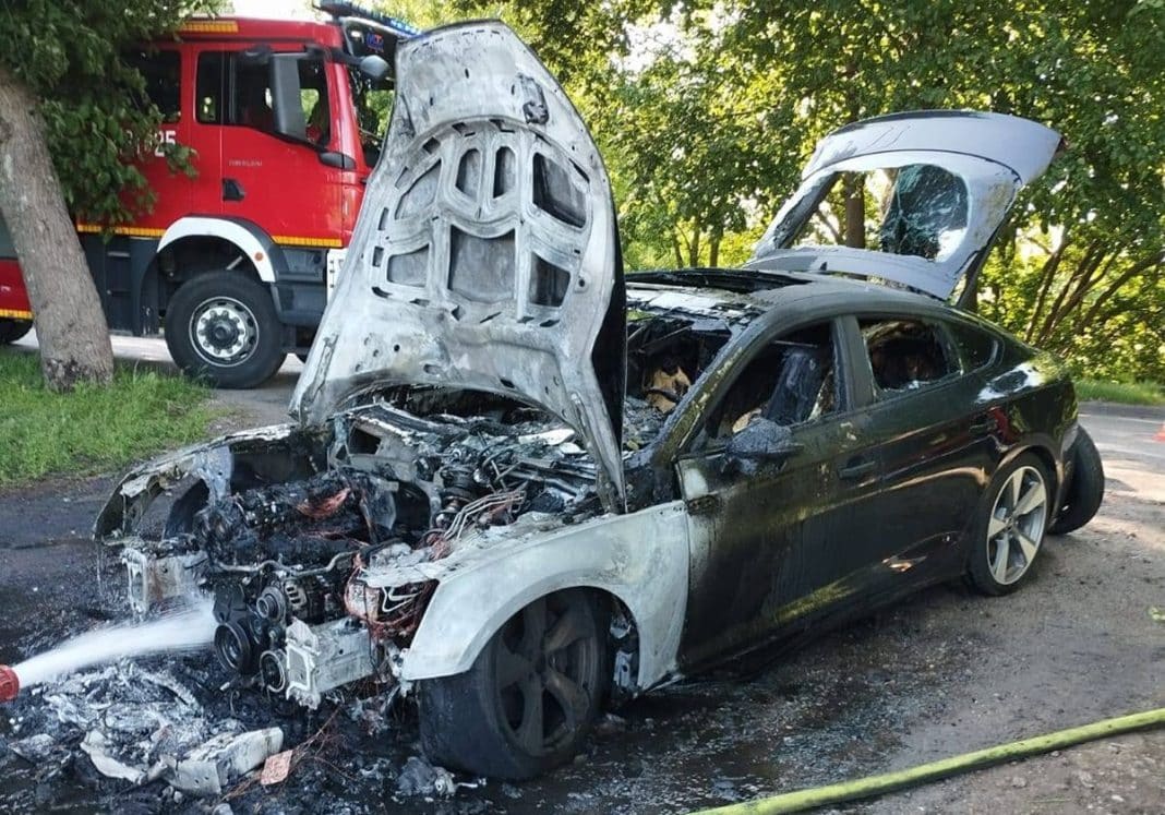 Spalony samochód marki Audi w miejscu zdarzenia, z widocznymi uszkodzeniami silnika i karoserii.