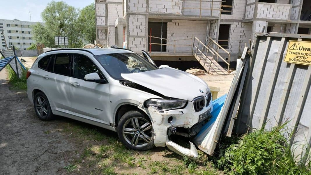 Samochód BMW wjechał w ogrodzenie placu budowy, uszkodzenia pojazdu widoczne na przedniej części.