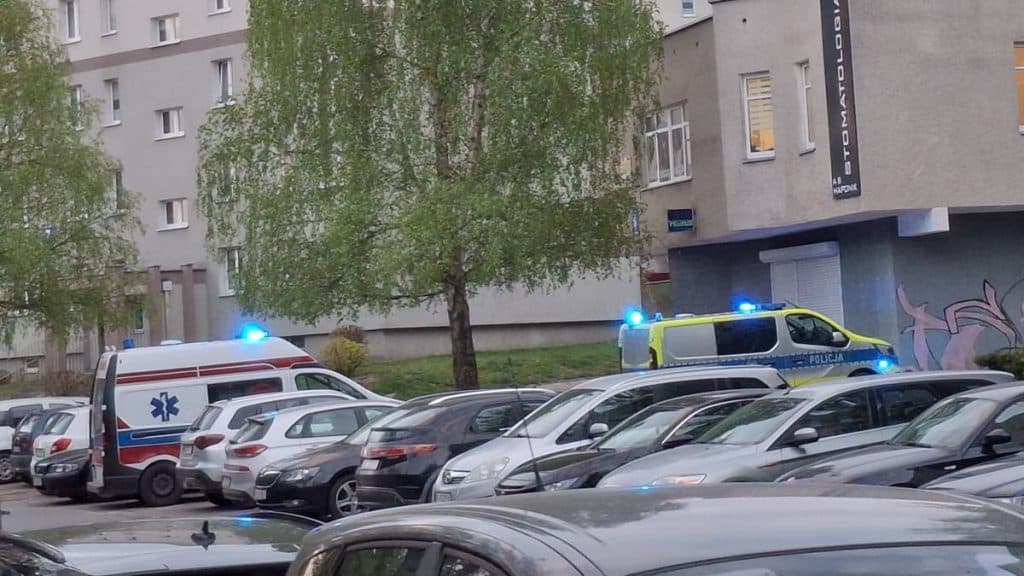 Widok na miejsce zdarzenia z karetkami i policją przed blokiem w Olsztynie.