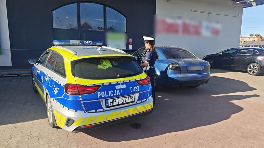 Policjantka rozmawia z kierowcą przy zatrzymanym samochodzie na parkingu.
