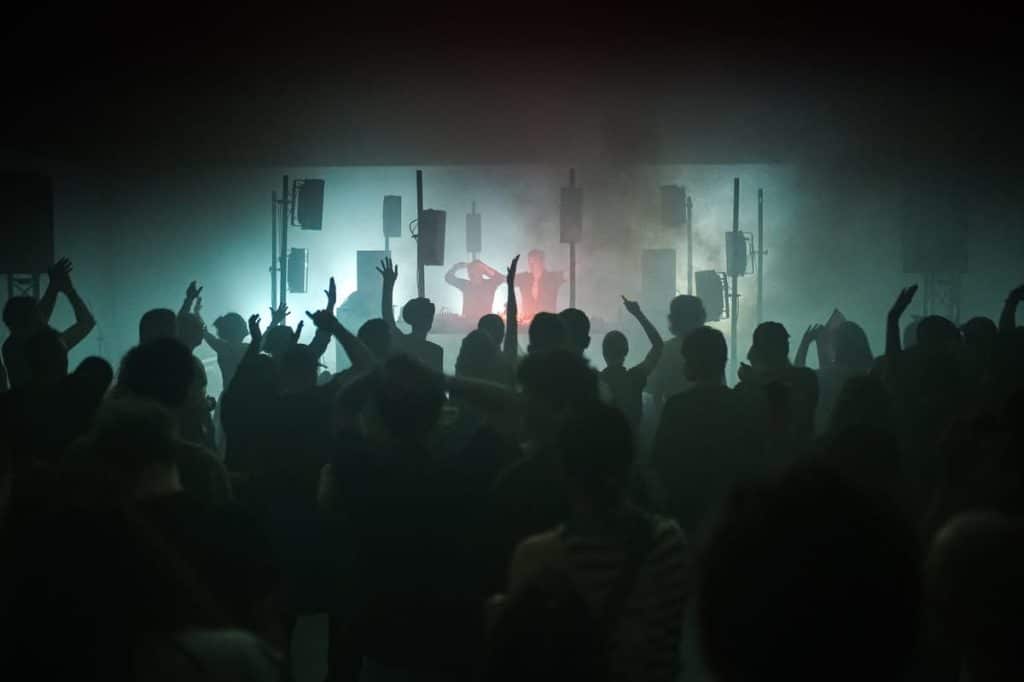 Tłum ludzi na festiwalu muzycznym z oświetleniem i DJ-em na scenie w tle.