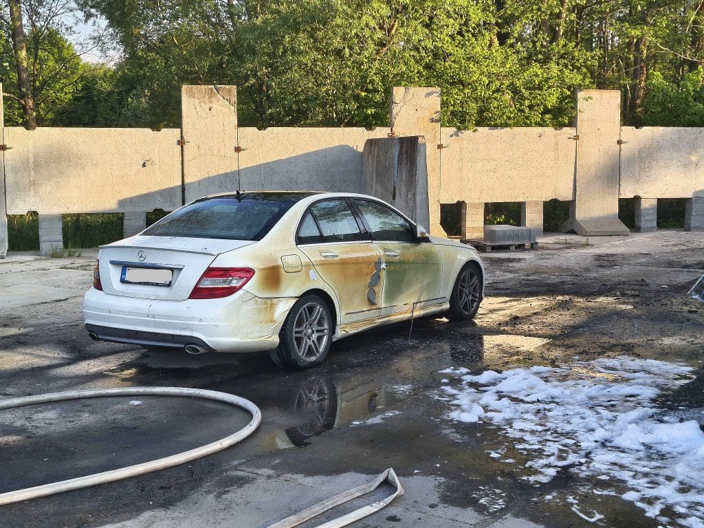 Uszkodzony samoch&oacute;d po pożarze na parkingu, widoczne ślady ognia i spalone powierzchnie.