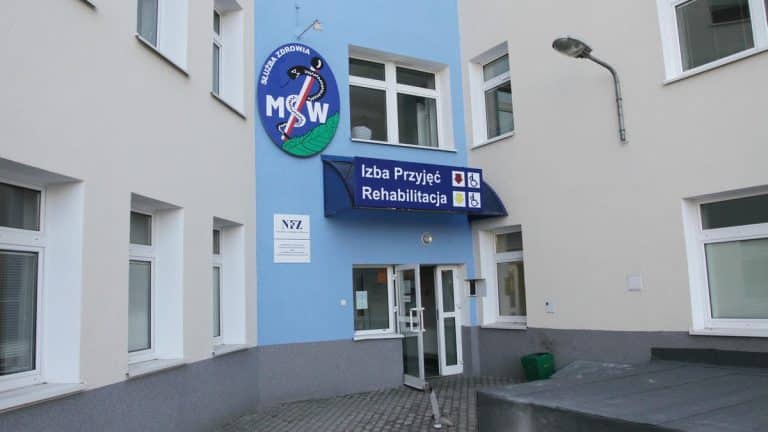 Widok z zewnątrz budynku szpitala z oznaczeniem izby przyjęć i rehabilitacji.