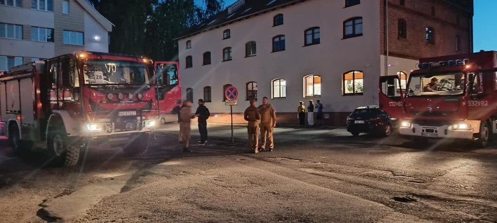 Strażacy z województwa warmińsko-mazurskiego na miejscu pożaru lasu pod Warszawą, obok dwóch czerwonych wozów strażackich.
