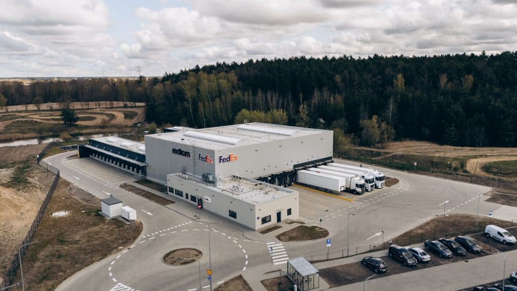 Nowe centrum logistyczne FedEx w Olsztynie, budynek z logo firmy i parking z samochodami.