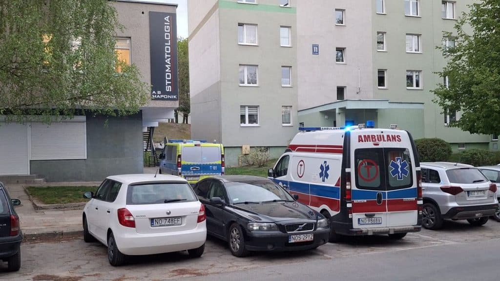 Widok na miejsce zdarzenia pod blokiem w Olsztynie, obecne pojazdy służb ratunkowych i policji.