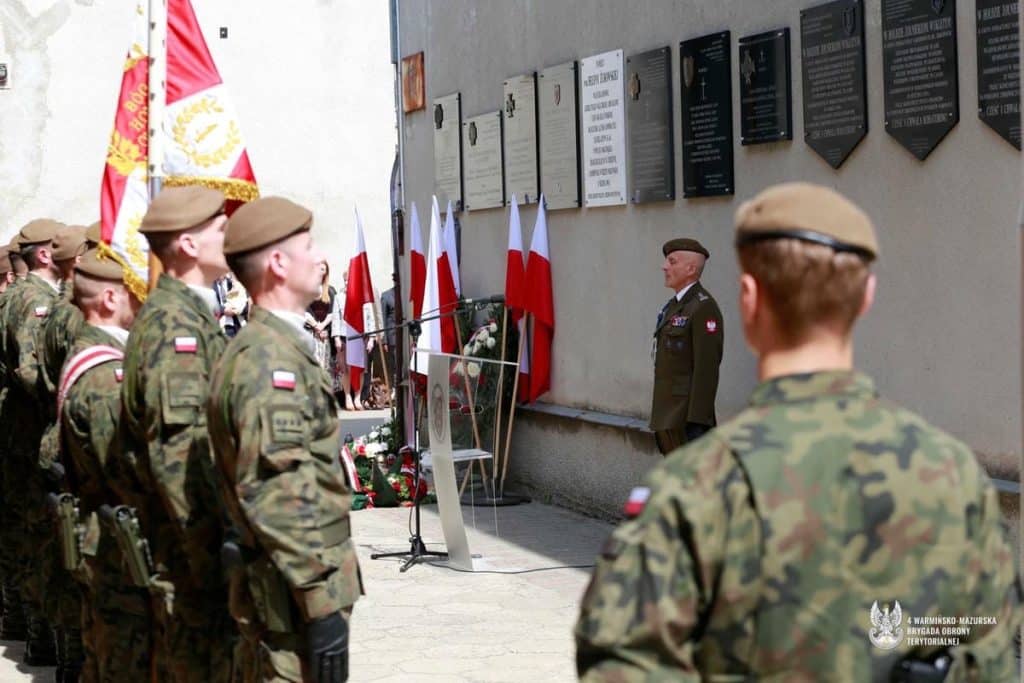 Żołnierze Obrony Terytorialnej podczas uroczystości pod pomnikiem, z flagami Polski w tle.