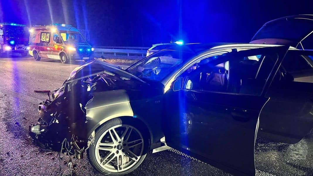 Rozbity samoch&oacute;d osobowy po wypadku na drodze S7, w tle służby ratunkowe z włączonymi światłami.