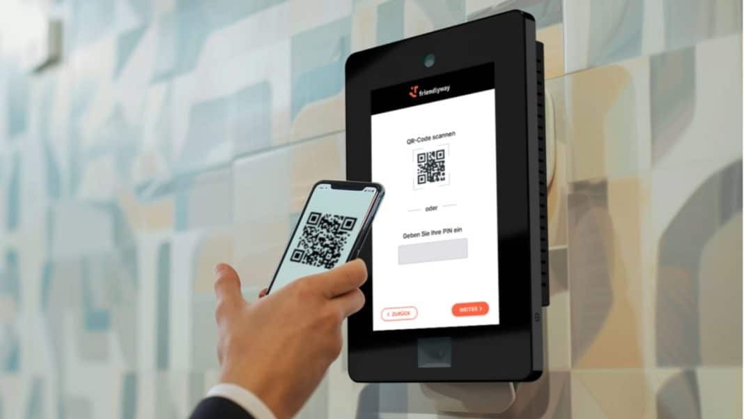 Osoba skanuje kod QR na ekranie czytnika przy wejściu do biura, korzystając z telefonu.
