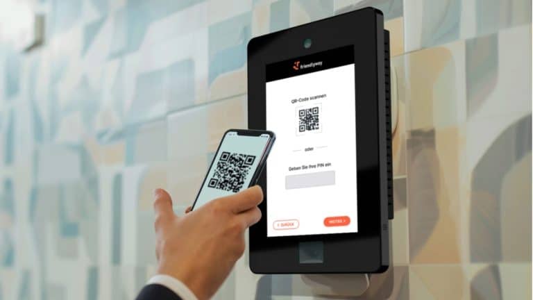 Osoba skanuje kod QR na ekranie czytnika przy wejściu do biura, korzystając z telefonu.
