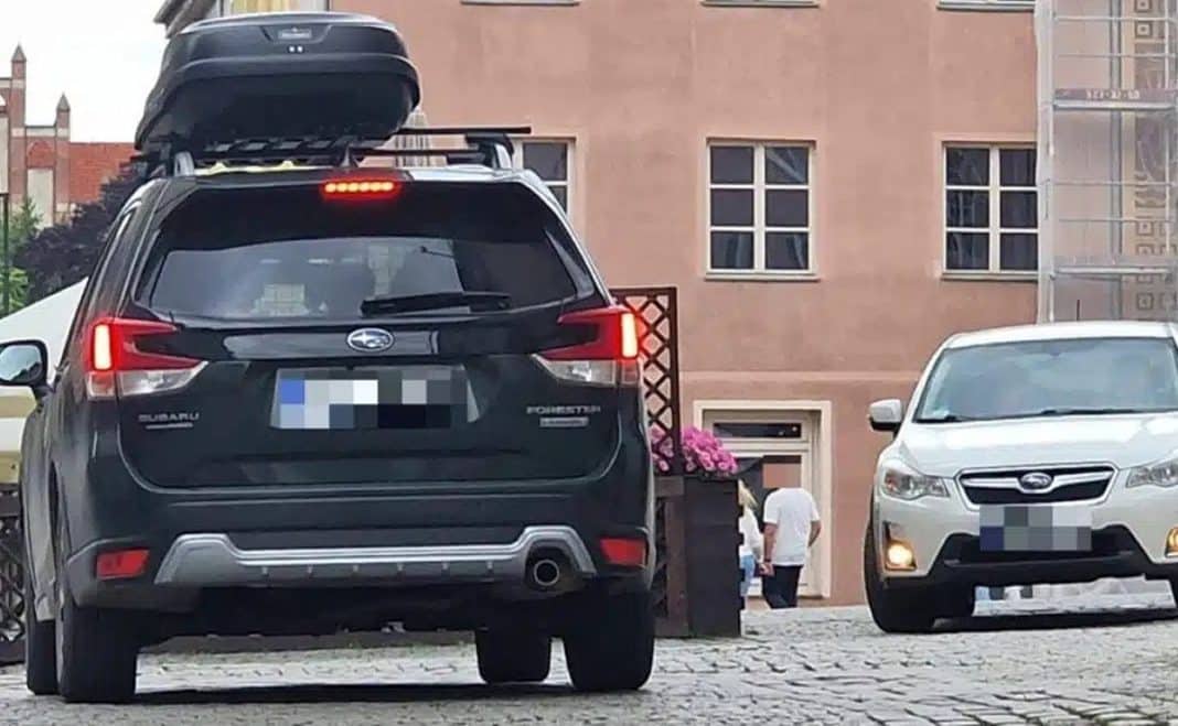 Samochody zaparkowane na brukowanym placu w centrum miasta, w tle budynek z oknami.