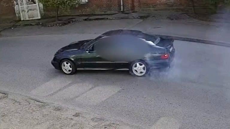 Czarny samoch&oacute;d podczas poślizgu na drodze, dym wydobywa się z opon.
