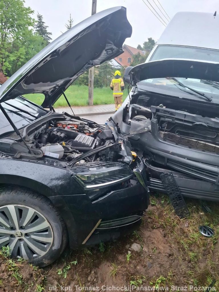 Zdjęcie przedstawia zderzone pojazdy na drodze powiatowej, z widocznym uszkodzeniem przodu samochod&oacute;w.