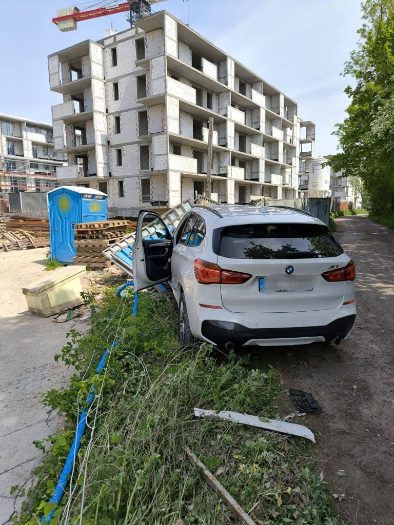 Samochód BMW wjechał w ogrodzenie placu budowy, uszkodzenia i elementy ogrodzenia na ziemi.