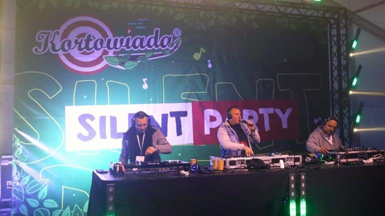 DJ-e na scenie podczas Silent Party z logo Kortowiady w tle, kolorowe światła i muzyka.