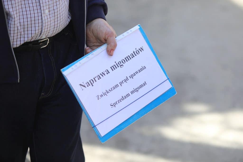 Osoba trzyma tablicę z informacją o naprawie migomatu na targu w Olsztynie.
