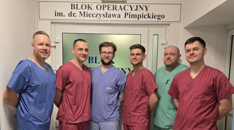 Grupa mężczyzn w uniformach pielęgniarskich stojąca przed wejściem do bloku operacyjnego w szpitalu.