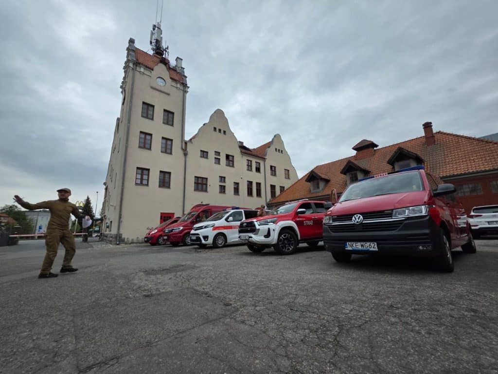 Strażak stojący obok pojazd&oacute;w ratowniczych przed budynkiem, nad chmurami.