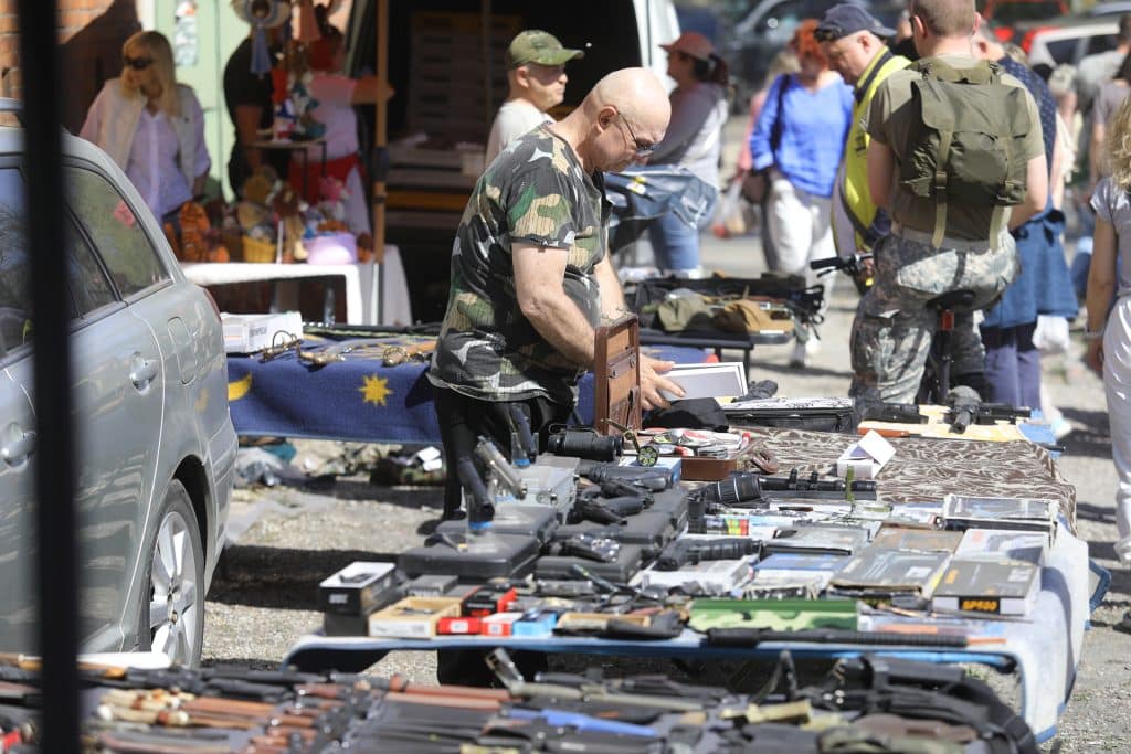 Sprzedawca na pchlim targu w Olsztynie, wystawiający r&oacute;żne przedmioty na stoisku, wok&oacute;ł tłum ludzi.