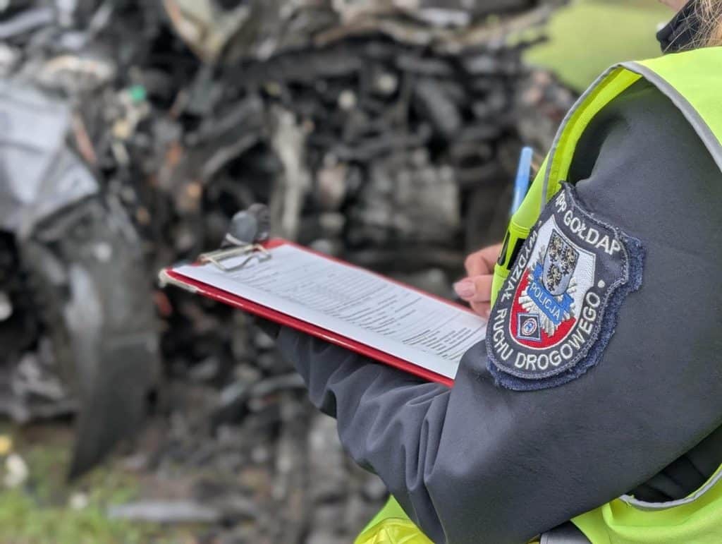 Policjant z notatnikiem przy wraku samochodu po wypadku w Skocze.