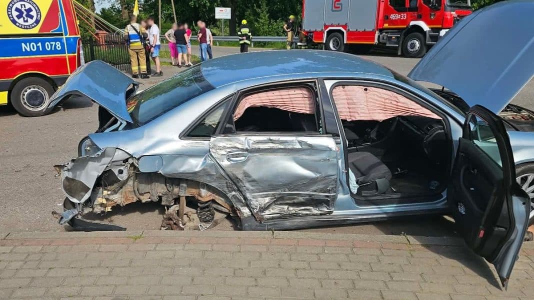 Uszkodzony samochód osobowy Audi po wypadku na drodze, z widocznym poważnym uszkodzeniem z lewej strony.