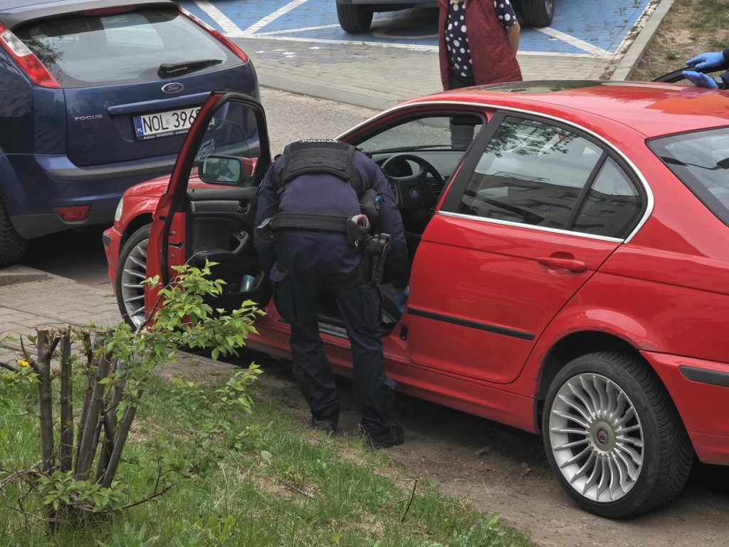 Policjant sprawdza samoch&oacute;d czerwonego BMW na parkingu w centrum Olsztyna.
