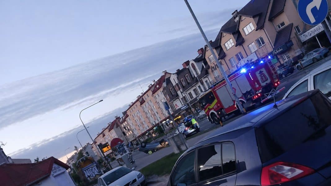 Wypadek na ul. Wilczyńskiego w Olsztynie, samochód przewrócony na bok, słupek i służby ratunkowe na miejscu.