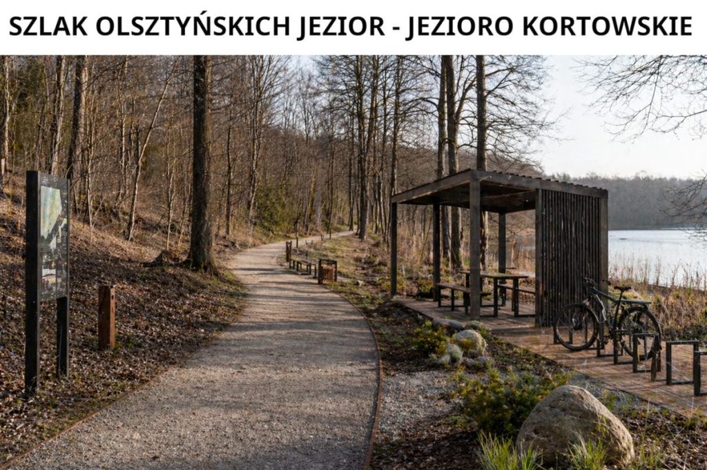 Ścieżka rowerowa nad jeziorem Kortowskim w Olsztynie, otoczona drzewami i infrastrukturą rowerową.