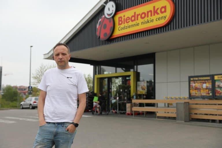 Mężczyzna stojący przed sklepem Biedronka w Olsztynie, na tle logo sklepu.