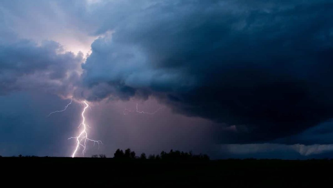 Burzowe niebo z ciemnymi chmurami i błyskawicą nad krajobrazem.