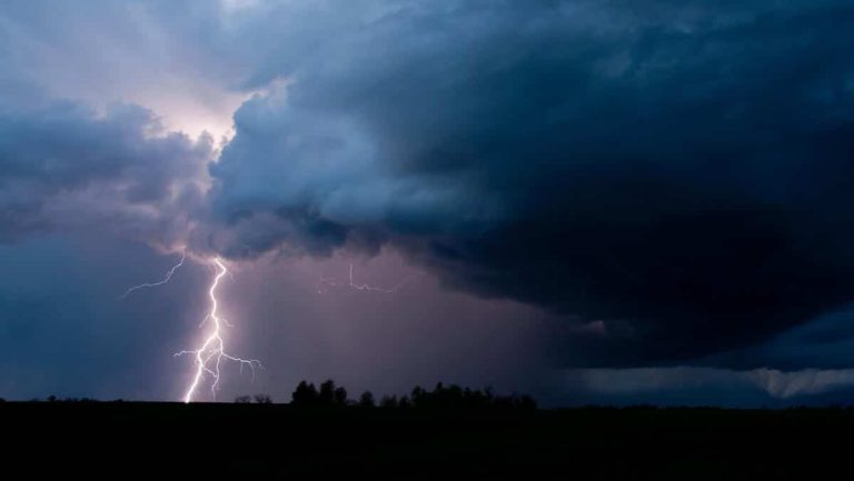 Burzowe niebo z ciemnymi chmurami i błyskawicą nad krajobrazem.