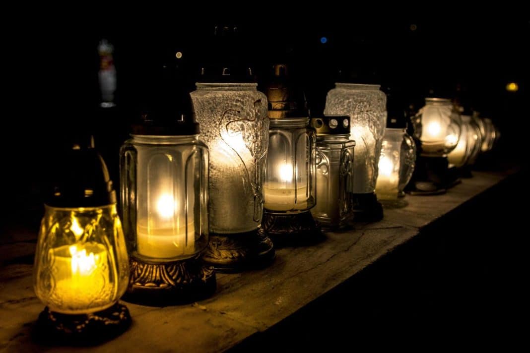 Na zdjęciu kilka lampionów z zapalonymi świecami ustawionych na drewnianym stole w ciemności.